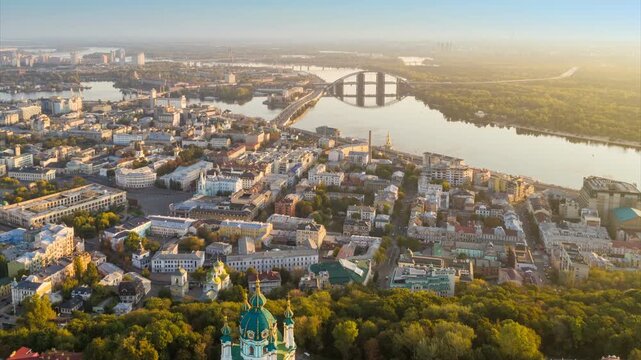 St. Andrew's Church on the hill in Podil district of Kyiv, beautiful aerial hyper lapse of Kiev city at sunrise. Golden morning sun rays over historic center of Kyiv, Dnieper river and bridges