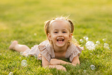 Fototapeta premium portrait of a little blonde girl in summer on a green lawn