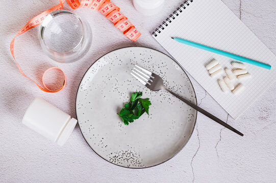 Parsley leaves and a fork on an empty plate, a notebook and capsules on the table top view