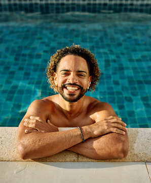 Portrait of a young man in a pool wearing swim shorts while smiling in warm weather during a sunny day at a leisure location