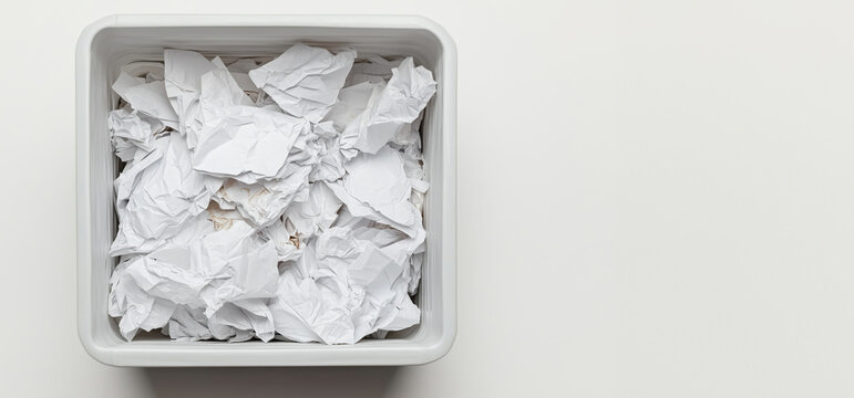 Crumpled paper pile in a square trash bin on a white background