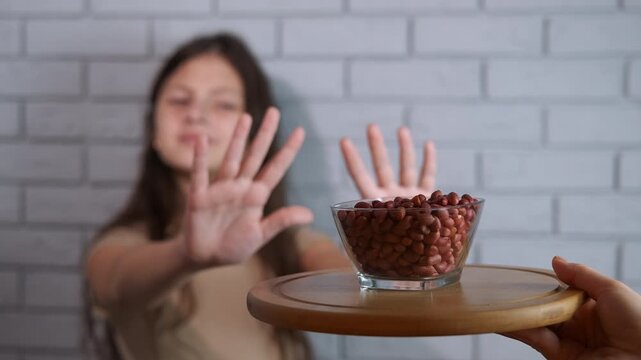 Young girl refusing a bowl of peanuts due to allergy. Unhappy young girl with a food intolerance showing a stop gesture with her hands. Symbolizing the concept of a dangerous allergic reaction