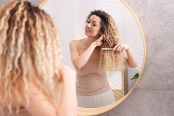 Obraz premium Unhappy woman trying to brush her tangled hair near mirror in bathroom