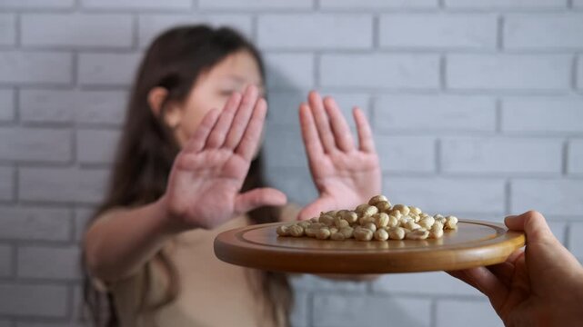 Teenager refusing to eat legumes showing a stop gesture. Young girl with a determined expression refusing of chickpeas or beans, making a stop gesture with her hands to show her food intolerance