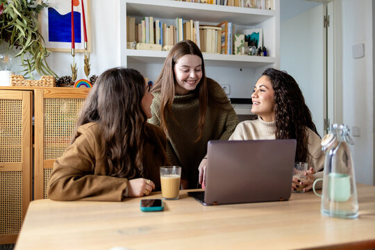 Happy friends laughing together during casual laptop time