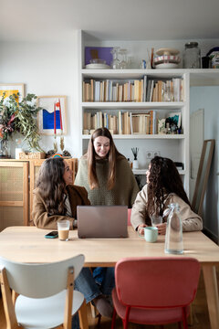 Friends laughing together while chatting around a laptop
