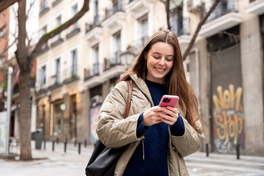 Young woman texting on smartphone while walking city street