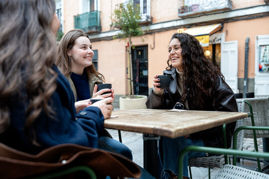Happy friends laughing with coffee at an outdoor cafe