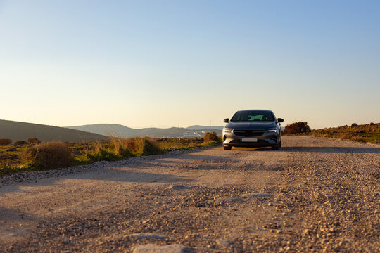 Car driving on gravel road at sunset in rural landscape