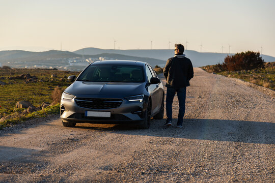 Man beside modern car on rural road at golden hour light