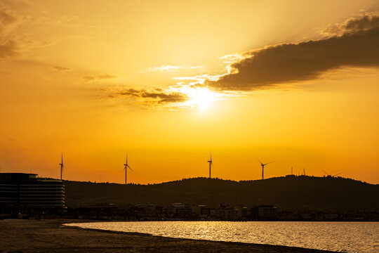 Golden sunset over coastal hills with wind turbine silhouette