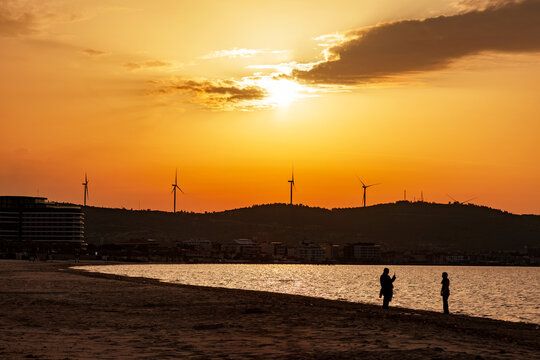 Sunset silhouettes on quiet beach with wind turbines