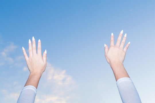 Gen Z girl raising hands to blue sky, freedom concept