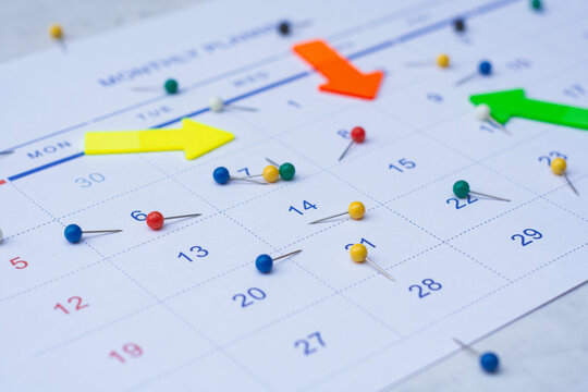 Business planning. Close up of a monthly planner calendar with colorful arrows and push pins marking important dates. Concept of scheduling, deadlines, task prioritization and time management.