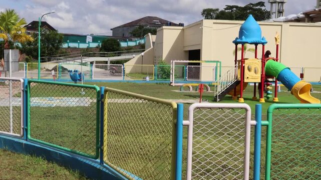 Balikpapan-Indonesia april 05, 2026 Colorful outdoor children's playground with slides and fences stands on a green lawn under a cloudy sky during the day, providing a safe recreational space in an ur