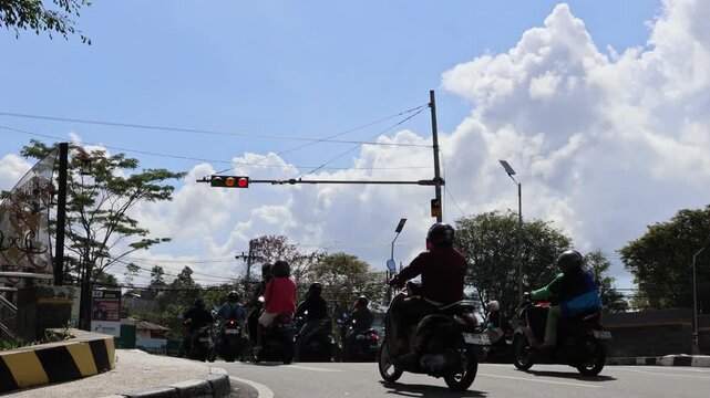 Balikpapan-Indonesia april 05, 2026 Vehicles and motorcyclists waiting at a red light intersection in a sunny city under green tree branches, capturing daily urban traffic flow during a bright day.