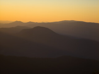 Obraz premium Layered mountain silhouettes fading into a warm golden sunset sky, captured from Ceahlău Massif in Romania.
