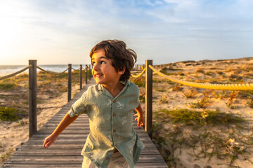 Joyful boy running on beach boardwalk at sunset