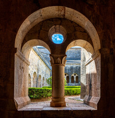 Le Thoronet Abbey cloister view, Provence-Alpes-Côte d’Azur, France : Romanesque arches framing courtyard with central column and blue sky