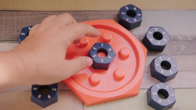 Hand placing numbered blue hexagonal puzzle pieces orange educational game board, developing logic and math skills, STEM toy, mental exercise, cognitive development, problem solving, matching numbers
