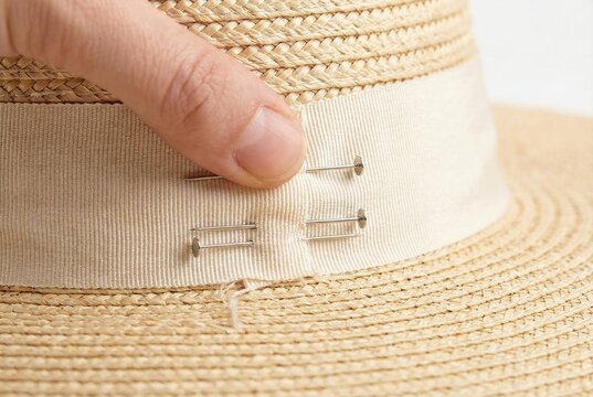 Milliner using metal pins to attach a beige ribbon to a handmade woven straw hat