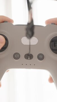Vertical video. Person Holding and Tilting FPV Drone Controller with Cable in Bright Backlight, Front Low Angle, Drone Operation Concept