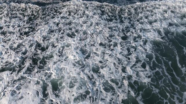 High-quality 4K drone footage at 29fps providing a mesmerizing zenith (top-down) view of the ocean. The fixed camera captures the rhythmic movement of calm waves crashing and dissipating on the shore 