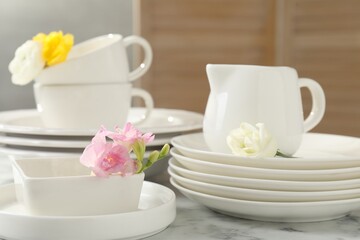 Fototapeta premium Many clean dishware and beautiful flowers on white marble table indoors, closeup