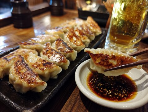 居酒屋のカウンターでビールと一緒に味わう焼き色のついた美味しそうな焼き餃子の写真