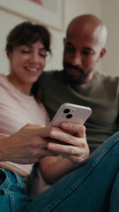 Fototapeta premium Couple Smiling on Sofa Using Smartphone Together