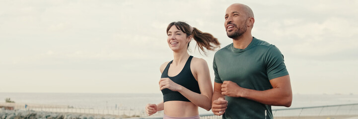 Fototapeta premium Running woman and man enjoy their summer morning workout. Team sports. Couple goals and motivation. Happy fit people are cheerfully doing sports. Panoramic