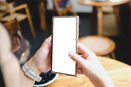 A close-up view of a person holding a smartphone with a blank white mockup screen while sitting in a cafe.