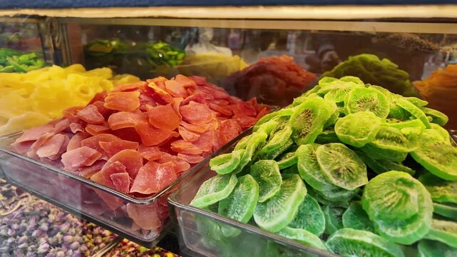 Assorted colorful dried fruits display in glass containers at market stall indoor footage.