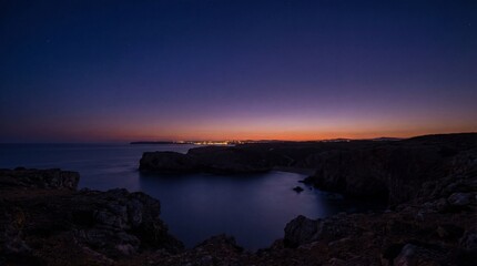 Fototapeta premium Boy stands in tall grass looking at night stars concept. Stunning twilight view of a calm ocean and rocky coastline.