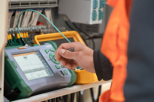 A technician diagnoses a problem area in a telecommunication network. The engineer in a white helmet measures the level of the optical signal in the server room of the data center