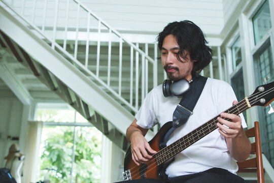 Handsome Japanese man with beard practicing electric bass guitar at home