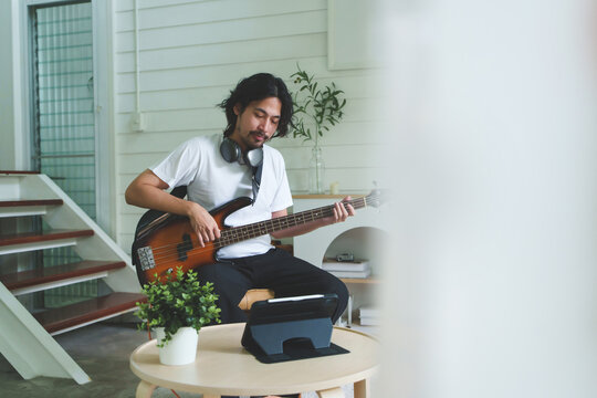 Japanese man using tablet to practice electric bass guitar online at home