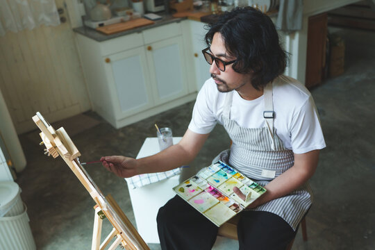 Japanese man relaxing and painting with watercolor on easel at home