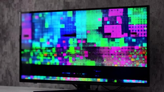 This shows a television screen with a vibrant and distorted pixelated error screen. The screen is displaying a chaotic mess of colors and pixels, indicating technical difficulties. The television is