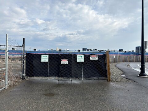 Construction Perimeter Warning: A chicken wire fence draped with a black privacy tarp features warning signs to redirect motorists around a work zone.