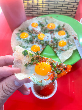 Close-up of banh trang nuong slice with quail eggs and toppings, dipped into a cup of red chili sauce