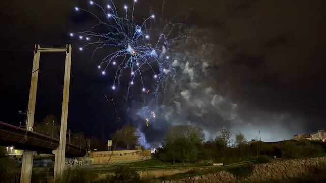 TIMELAPSE | Fireworks illuminating the night sky over a bridge and river, creating colorful reflections during the traditional Fallas de Valencia festival