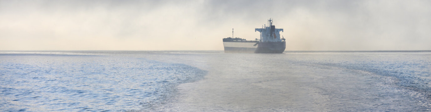 Bulk carrier cargo ship in Puget Sound on a foggy morning with air full of exhaust and pollution, global shipping of trade goods worldwide, import and export in the international economy
