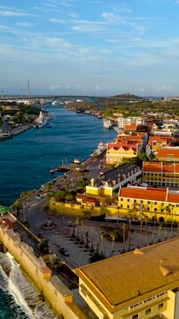 Vertical HD drone view of Willemstad harbor entrance at sunset showing Queen Juliana Bridge and the Punda waterfront.