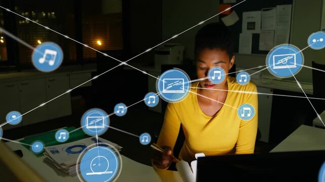 Woman working at desk, monitor emitting blue icons forming media network while writing and eating