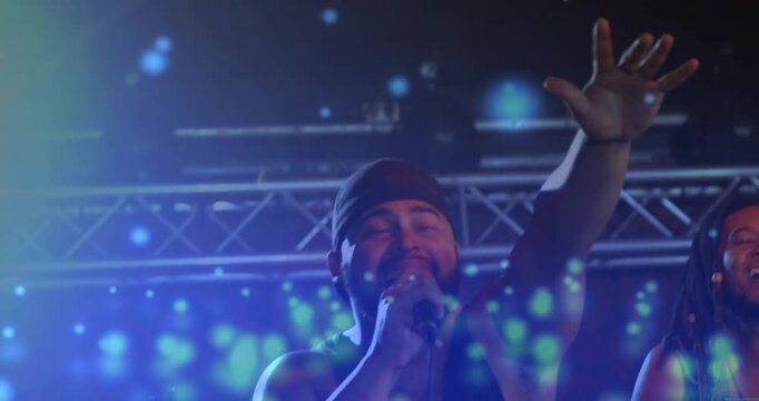Camera centering on lead singer, raising arm, holding wired mic, performing music with blue overlay