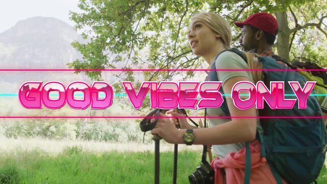 Hiking duo reaching tree edge pausing, viewing peak neon pink GOOD VIBES ONLY text framing hikers