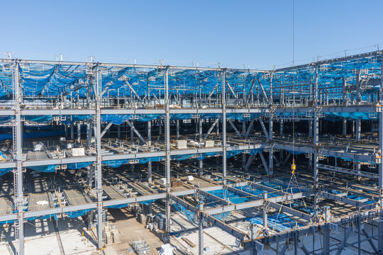 大規模鉄骨建築工事の全景と仮設足場・梁本締め作業の現場