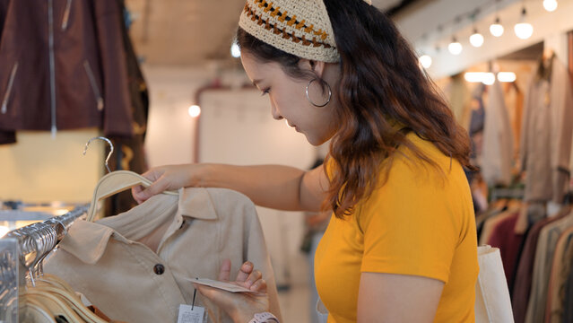 Young teen tourist Gen Z asia female choose look at zero waste eco go green buy second hand sale store flea market thrift old used vintage fabric style. Happy woman city asian people small retail shop