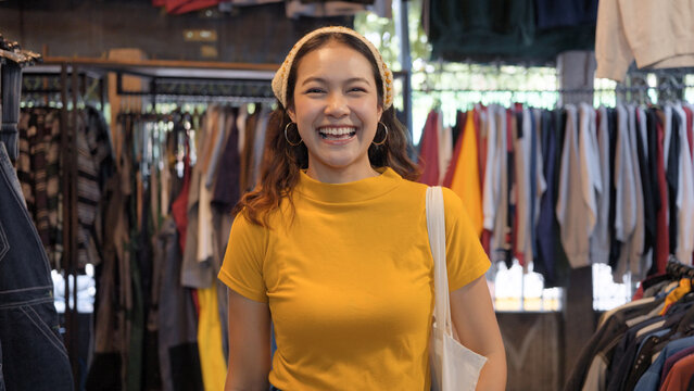 Young teen Gen Z asia female happy smile looking at camera at zero waste eco go green buy second hand sale store flea market mall thrift old used vintage fabric retro style. Woman people enjoy shop.